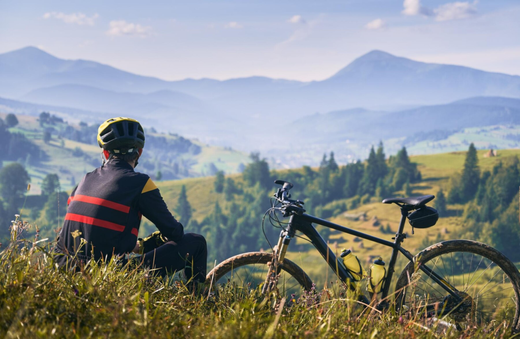 En cyklist sittande bredvid sin cykel och som blickar ut mot öppna landskap